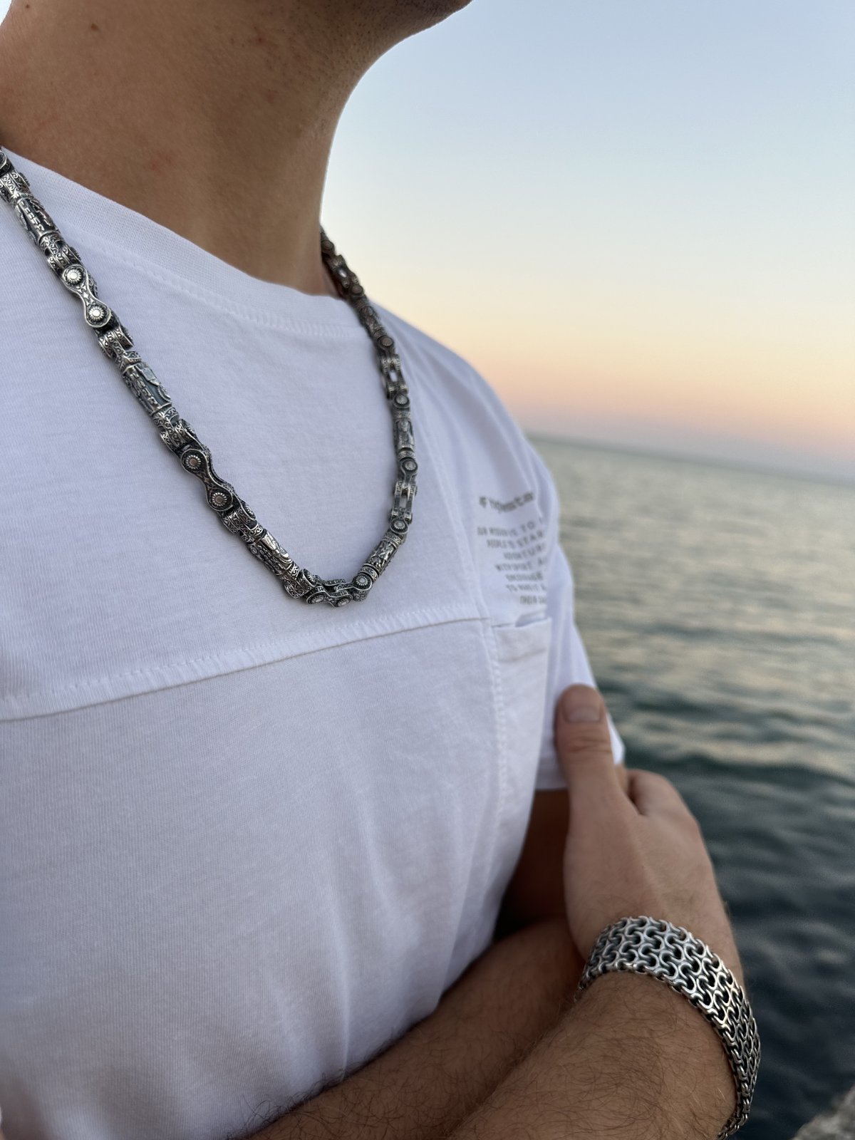 Massive silver chain and bracelet on a man against the sea background.