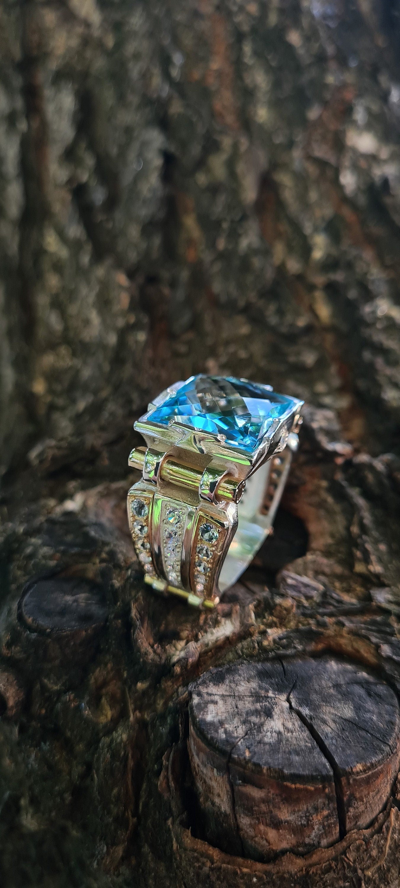 Large silver 925 men's ring with 14K gold accents and natural 15mm topaz against the background of a tree